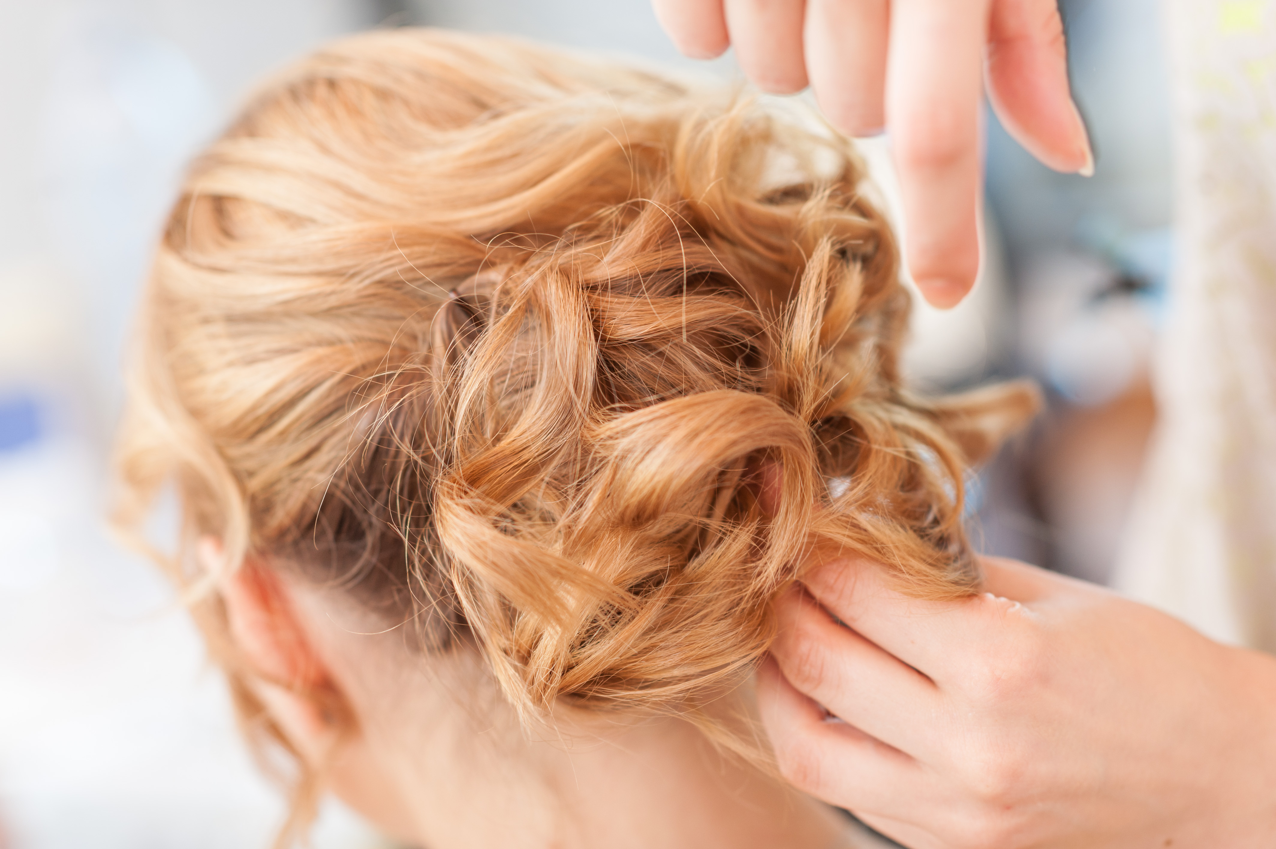 Image of a hair stylist inserting hair pins into a model's curled and pulled back hair.